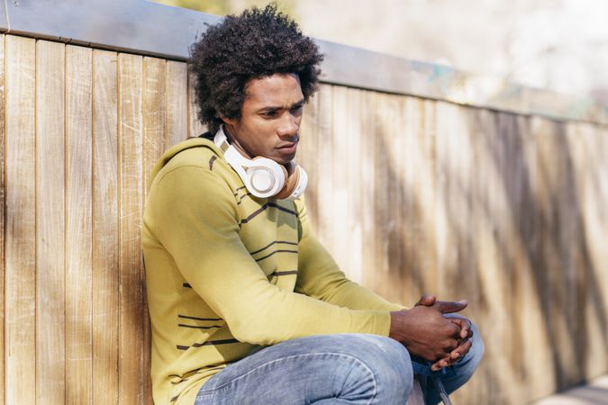 Unhappy man crouched with back against the wall outside