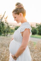 Young expecting woman in white dress standing in field