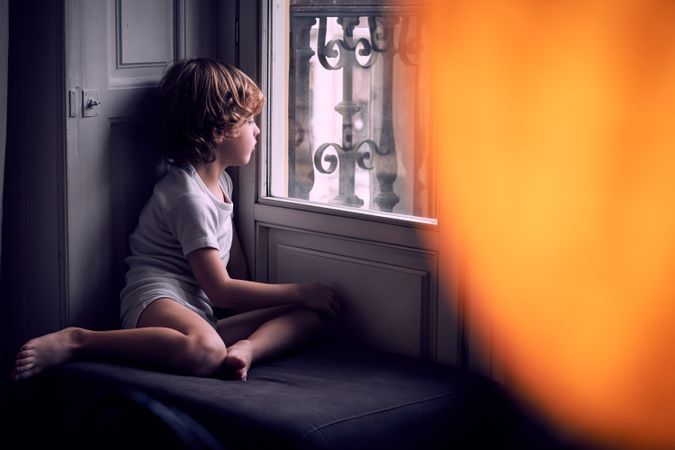Attentive kid looking through window at home