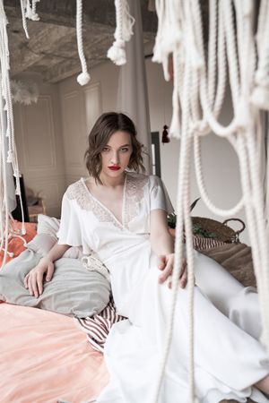 woman with red lips in white dress looking at camera while sitting on floor beside sofa