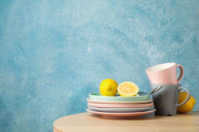 Plates and cups with lemons stacked on wooden table, space for text
