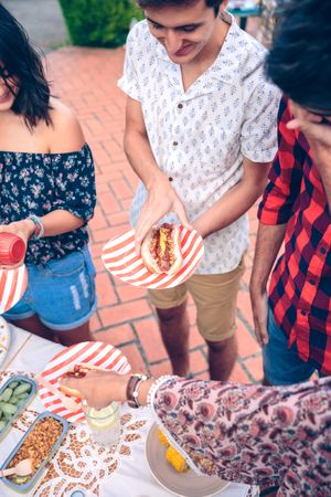 Young man holding hot dog at a barbecue with friends