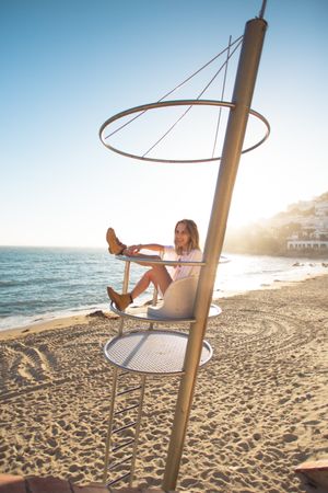 Beautiful blonde model sits atop guard tower on beach overlooking the coast