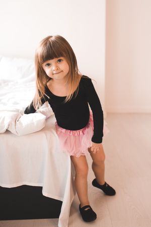 Girl in pink tutu standing beside bed