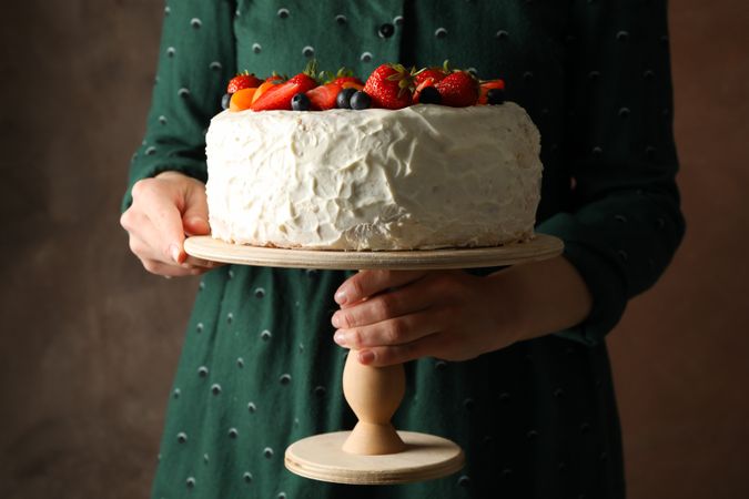Woman holds berry cream cake against brown background. Delicious dessert