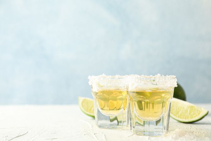 Tequila shots with salt and lime slices on light background