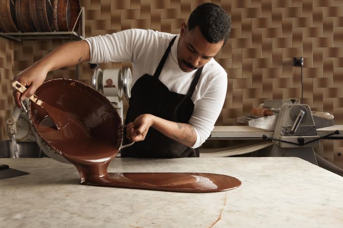 Professional chef in apron pouring melted chocolate onto counter