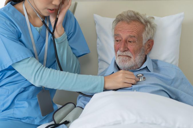 Asian nurse using stethoscope checking on heartbeat examining of older man
