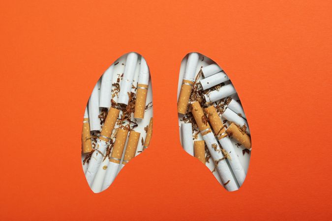Lung shape cut out of orange paper with cigarettes
