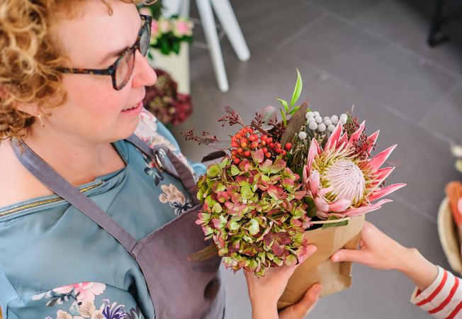 Female florist in eyeglasses selling flowers to client