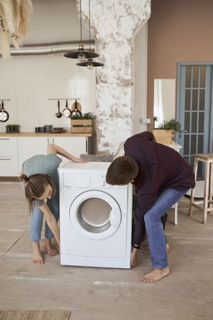 Enthusiastic couple carrying washing machine into new kitchen