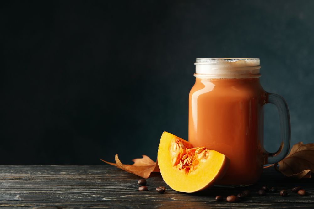 Glass jar of pumpkin latte, coffee seeds and leaves on wooden background