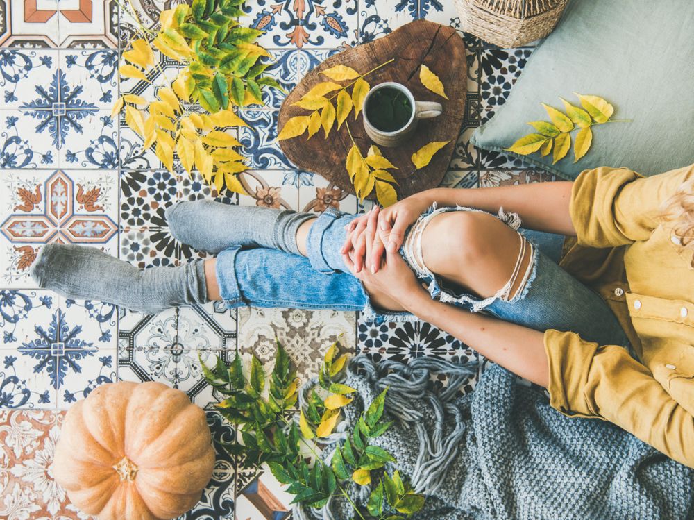 Woman sitting on colorfully tiled balcony with fall leaves and mug
