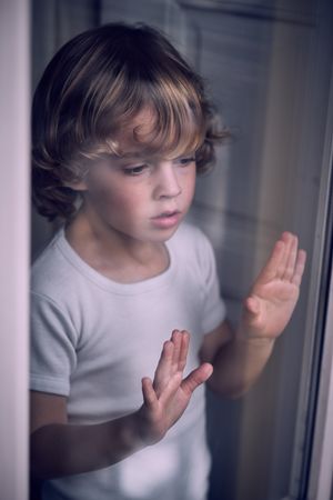 Attentive little child looking out window through glass