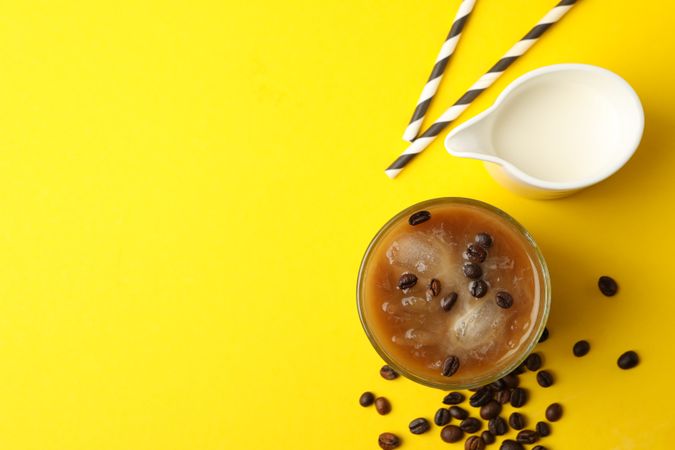 Glass of ice coffee on yellow background. Fresh drink