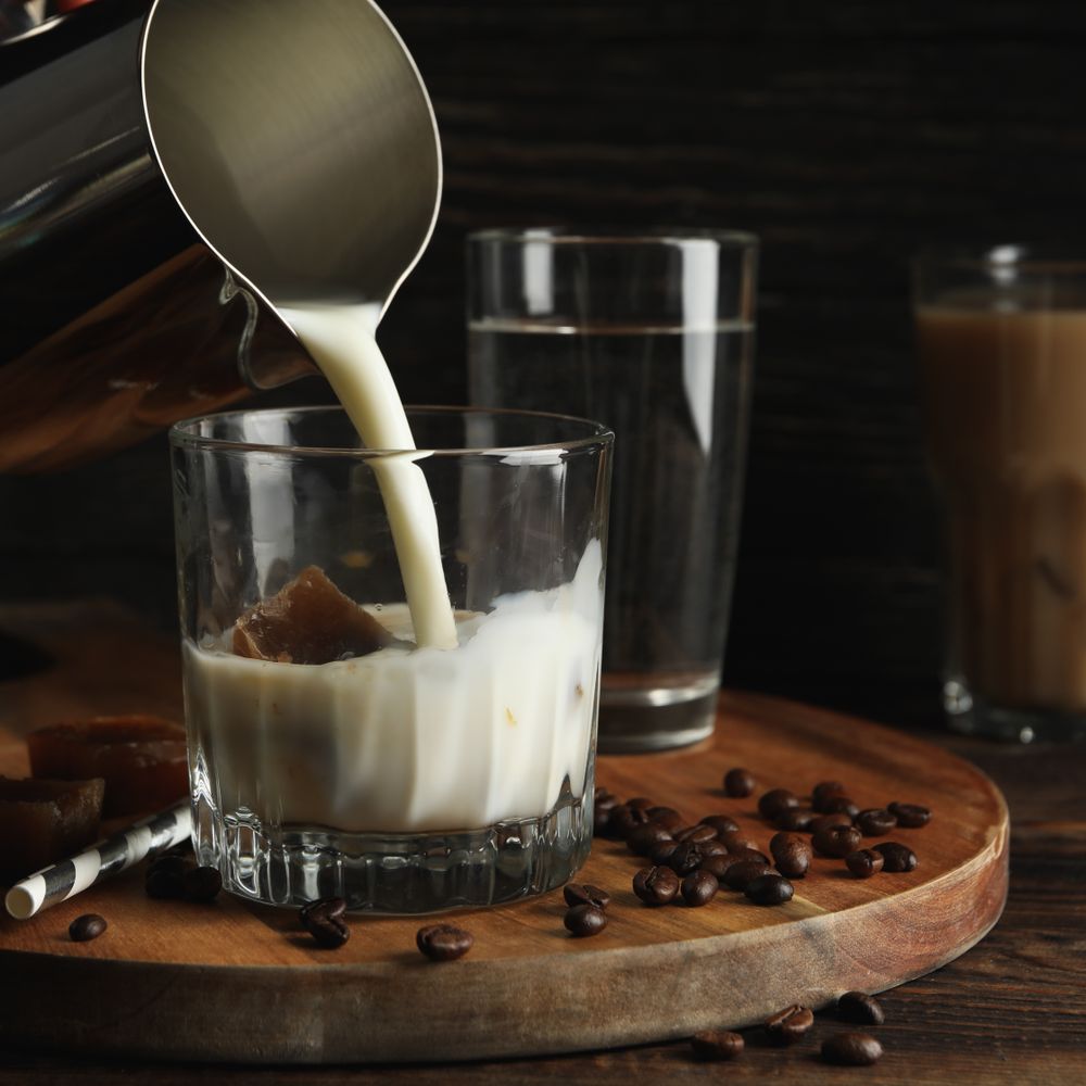 Milk is poured into a glass of coffee. Composition with ice coffee