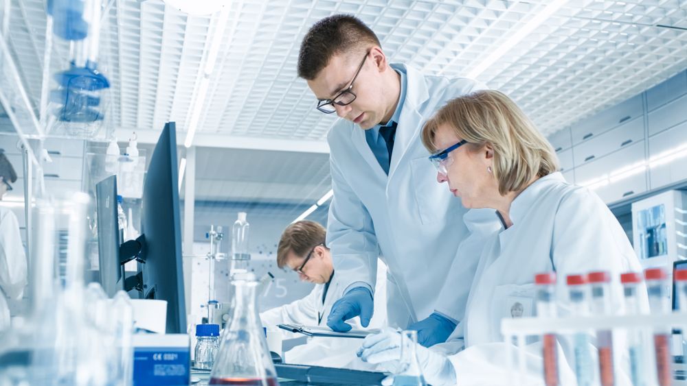 In Modern Laboratory Mature Female Scientist Has Discussion with Young Male Laboratory Assistant.