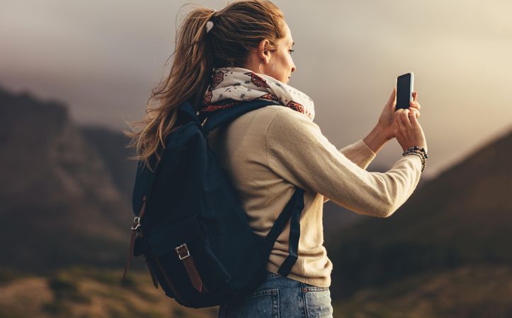 Young woman taking pictures of beautiful landscape with her smart phone