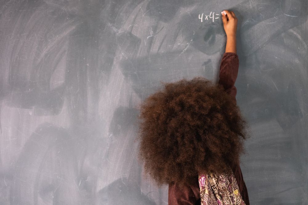Black girl writing on chalkboard in classroom