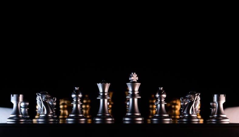 Silhouetted silver chess set with golden backdrop.