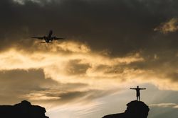 Human silhouette on hill delighting in view of aircraft in sky