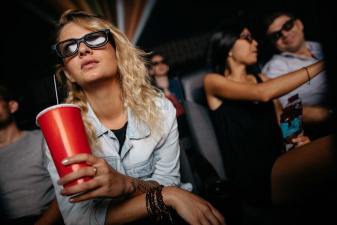 Young woman with cold drink and 3d glasses watching movie in theater