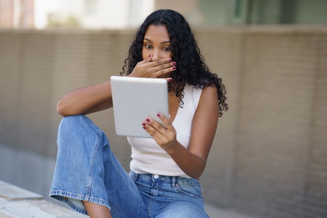 A Surprised Young Woman Engaging with a Tablet While Sitting in a Beautiful Outdoor Setting