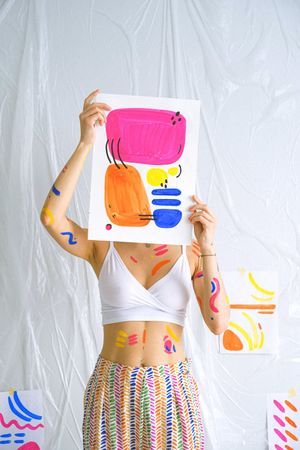 Woman in crop top and colorful skirt holding a watercolor painting