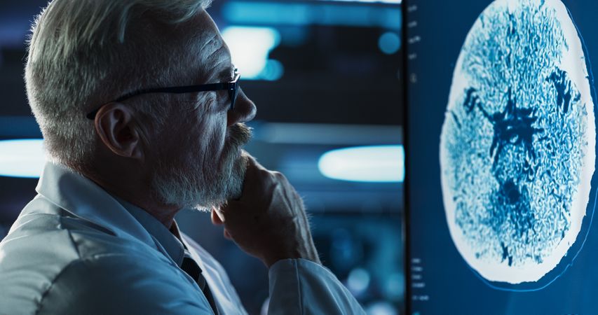 Medical Hospital Research Center: Close-Up Portrait Of Male Neurologist, Neuroscientist, Neurosurgeon, Looks at TV Screen with Brain PET Scan Images.