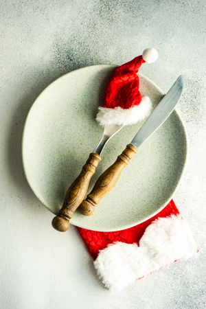 Cutlery setting with red Santa hat on silverware on pastel green background