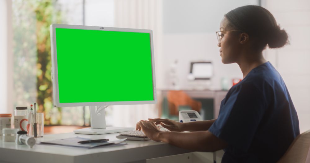 Portrait of a Black Female Medical Health Care Professional Working on Desktop Computer with Green Screen Mock Up Display in Hospital Office.