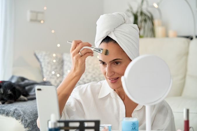 Smiling woman with smartphone applying makeup
