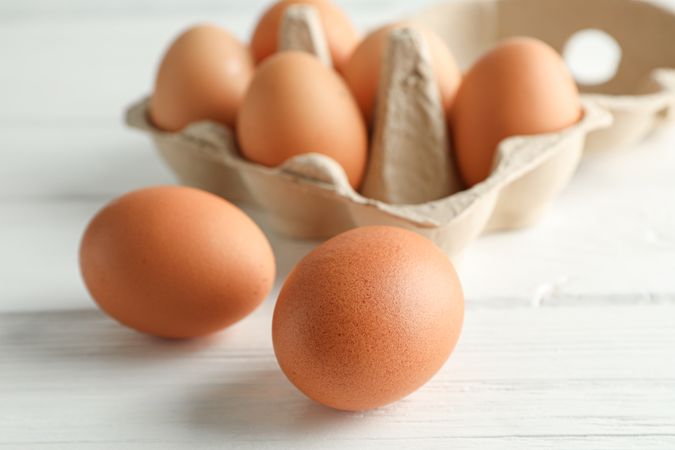 Brown chicken eggs in carton box on light background, space for text and closeup