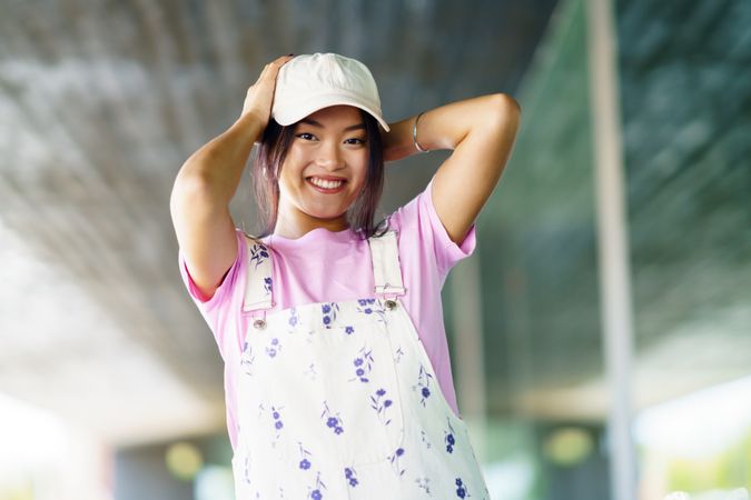 Happy female in floral overalls fixing cap on her head