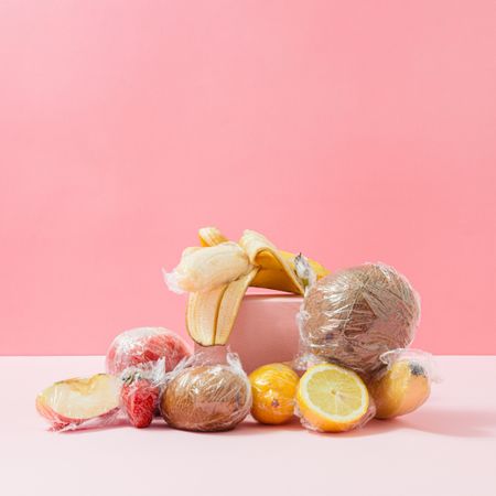 Plastic wrapped fruit on pink background