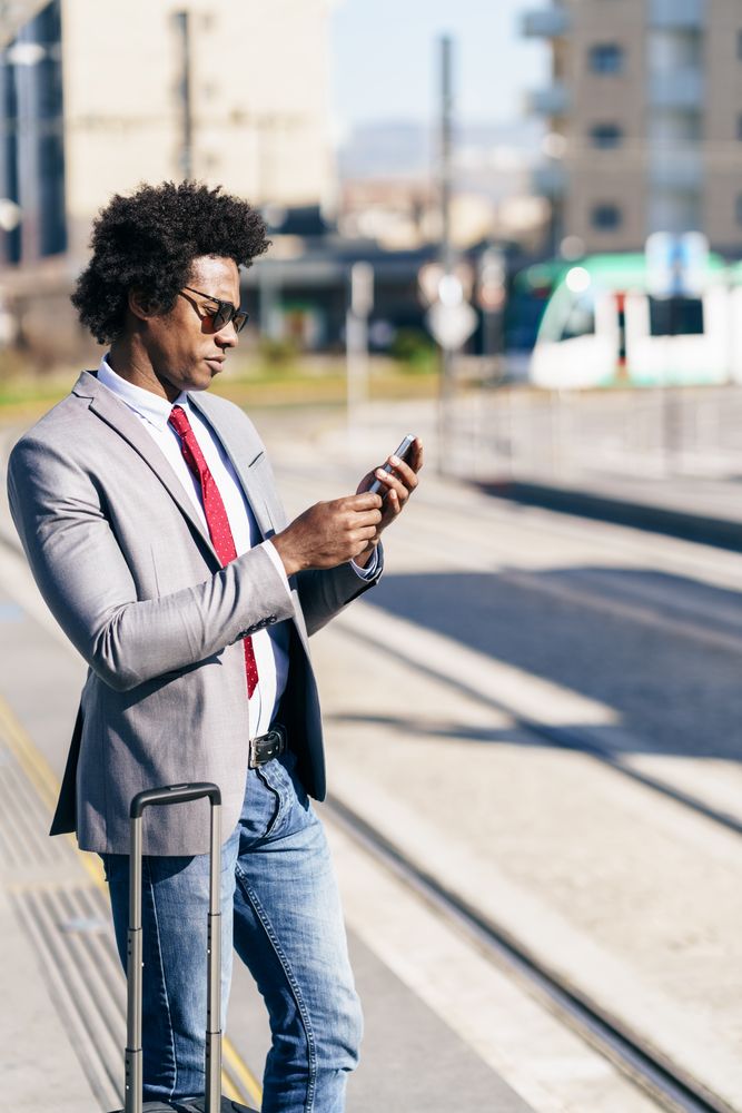 Man in jeans and dress shirt with tie standing outside with small suitcase