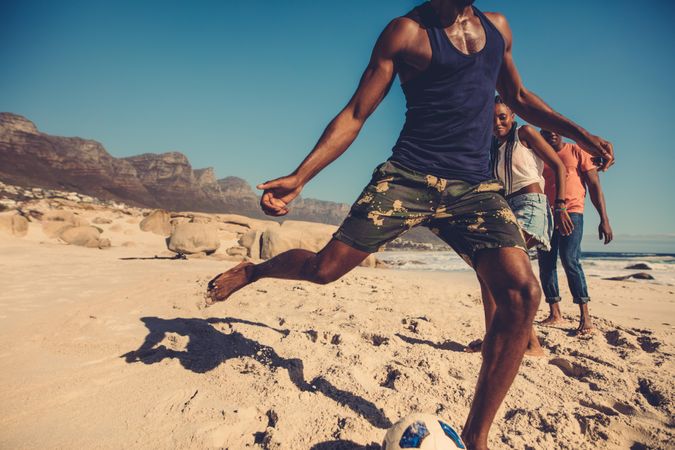 Man’s leg going in for a kick with a soccer ball on the beach