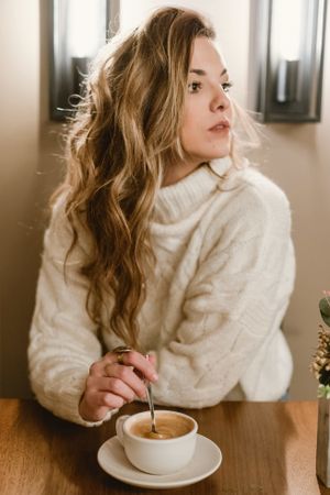 Elegant woman mixing coffee in cafe