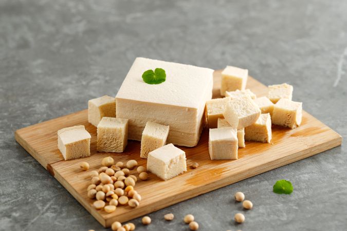 Block of cut tofu on breadboard with soybeans