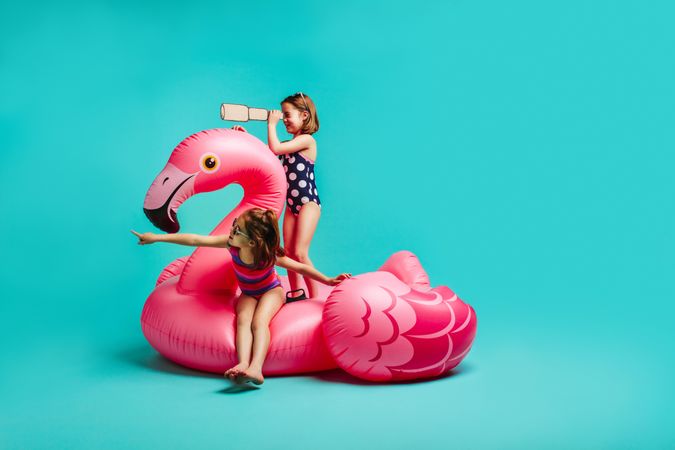 Two girls on inflatable toy flamingo with binoculars