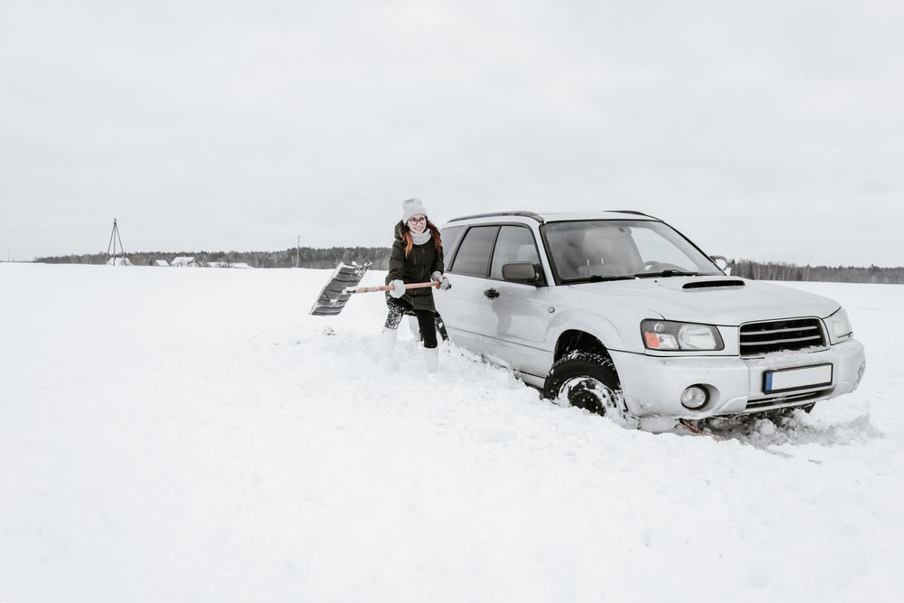 Woman with shovel near car on snow field