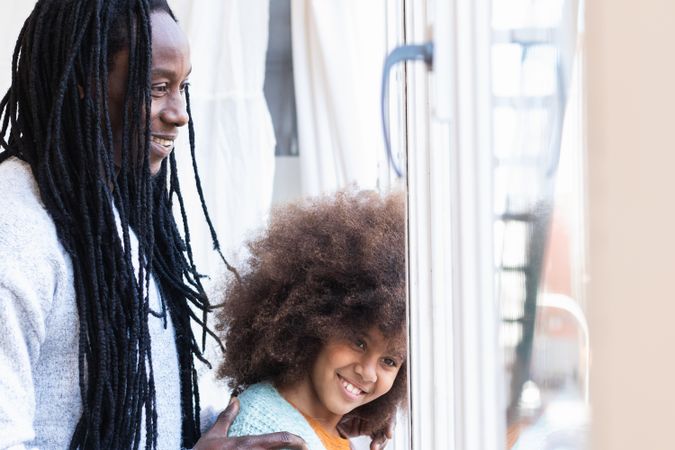 Black father with daughter standing near window