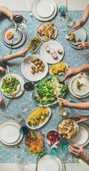 Group of people at blue patterned table with fresh fruits, salad, and vegetables, narrow composition