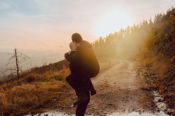 Smiling man holding cheerful guy on road on hill