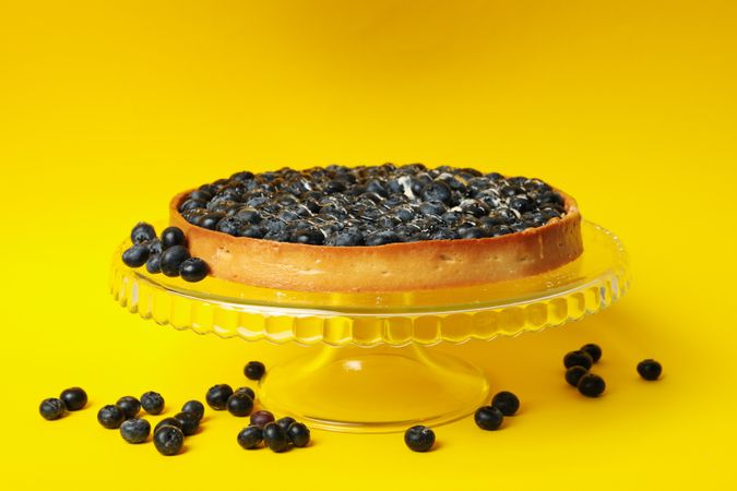 Glass stand with blueberry pie isolated on yellow background
