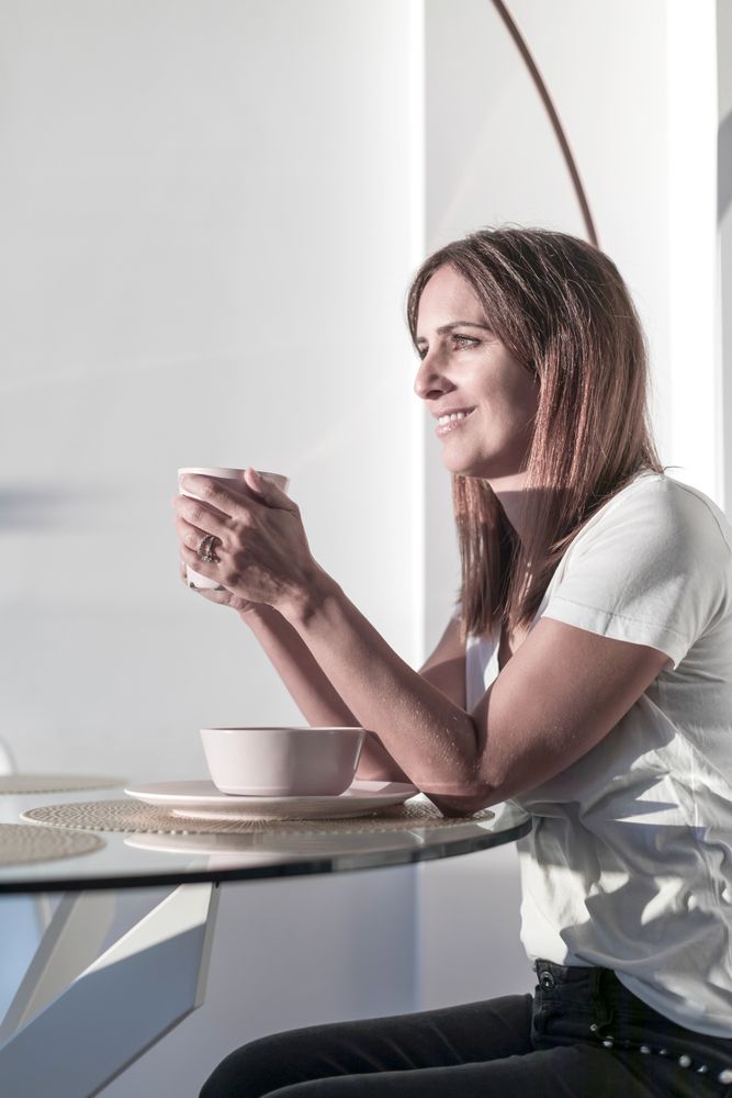 Smiling adult woman sitting at sunny table holding a cup of tea
