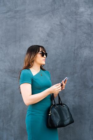 Chic female in blue dress standing outside with phone