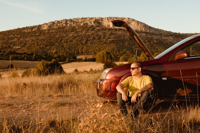 Man leaning in broken car in countryside