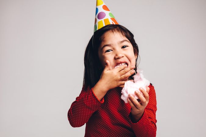 Young girl enjoying candy while wearing party hat