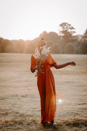 Woman in an orange dress holding flowers in a grassy field